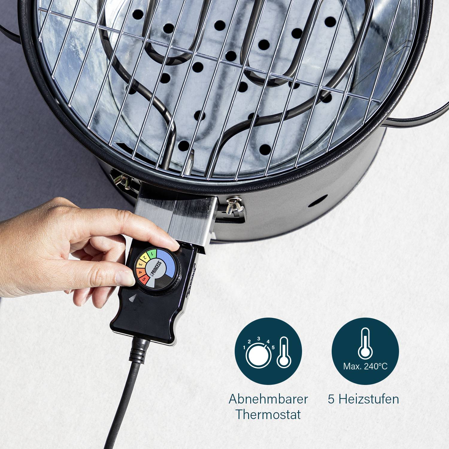 Hand dreht Thermostat an einem runden, silbernen Grill mit abnehmbarem Thermostat und fünf Heizstufen bis maximal 240°C.