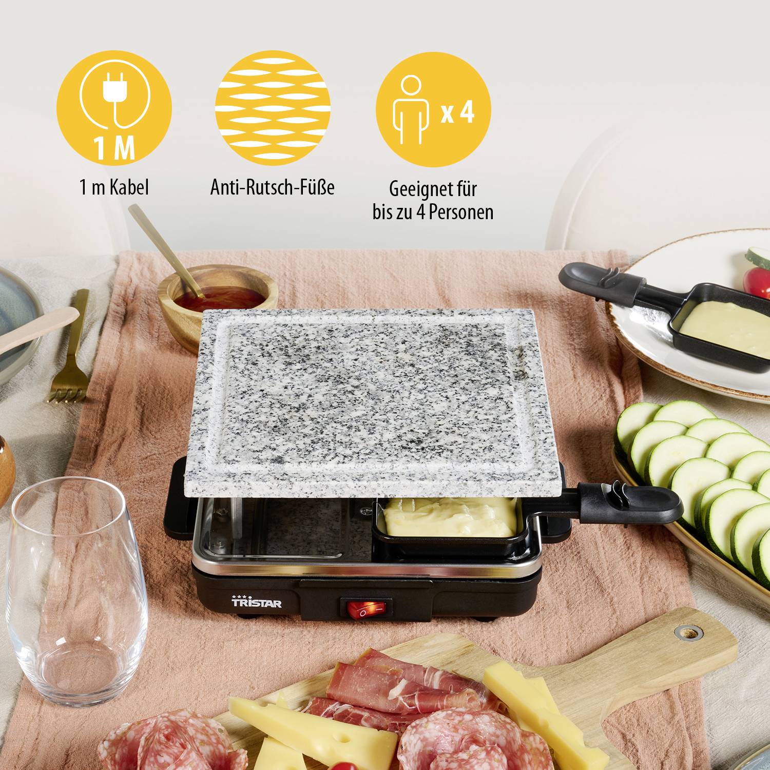 Tisch mit Raclette-Grill, Steinplatte in der Mitte. Zutaten: Zucchini, Fleisch, Käse, vier Raclette-Pfännchen. Geeignet für 4 Personen, 1 m Kabel.