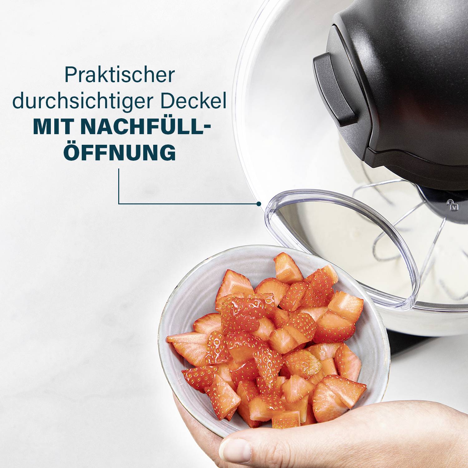 Eine Hand hält eine Schüssel mit geschnittenen Erdbeeren. Daneben ein Topf mit durchsichtigem Deckel und Nachfüllöffnung.