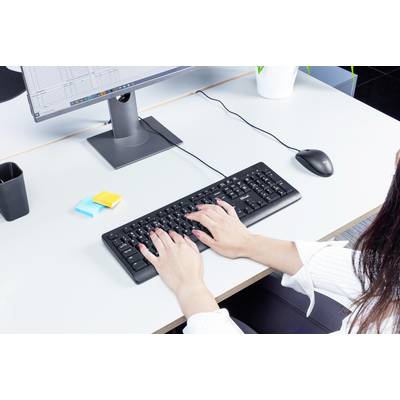 Eine Person tippt auf einer Tastatur an einem Schreibtisch mit einem Monitor. Auf dem Tisch liegen Klebezettel und ein Stift.