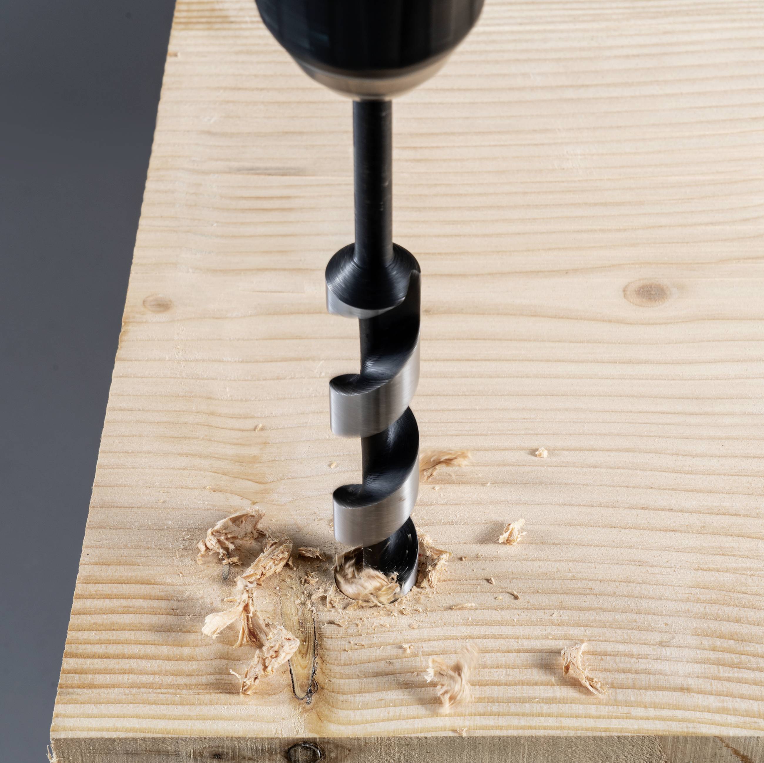 Ein Spiralbohrer bohrt in ein Holzbrett, Späne sind um das Bohrloch verteilt.