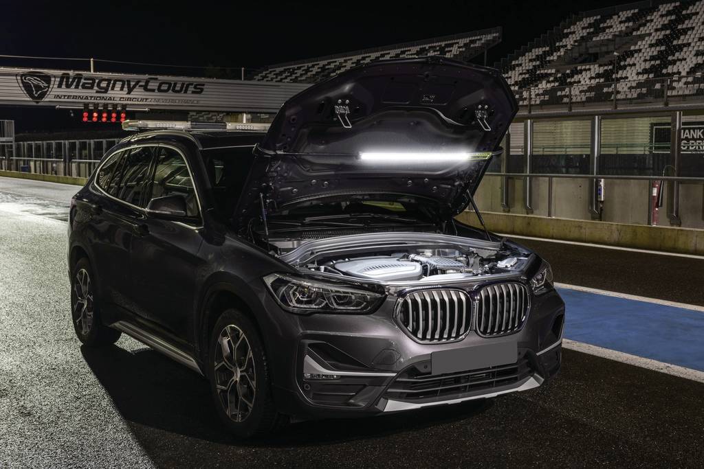 Ein Auto steht mit geöffneter Motorhaube auf einer beleuchteten Rennstrecke bei Nacht.