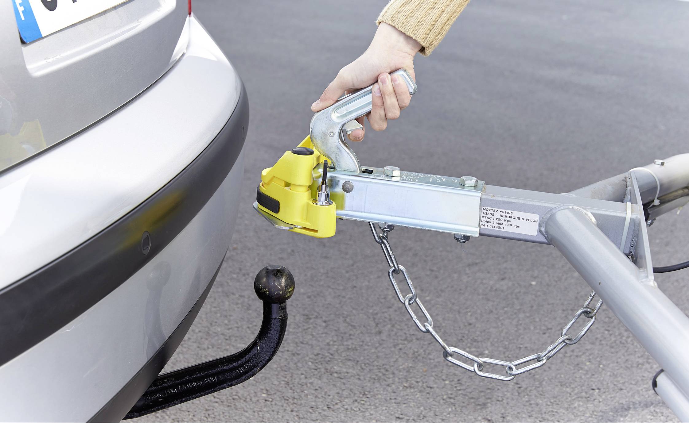 Eine Hand schließt eine Anhängerkupplung an die Anhängerkugel eines Autos an, um den Anhänger zu verbinden.