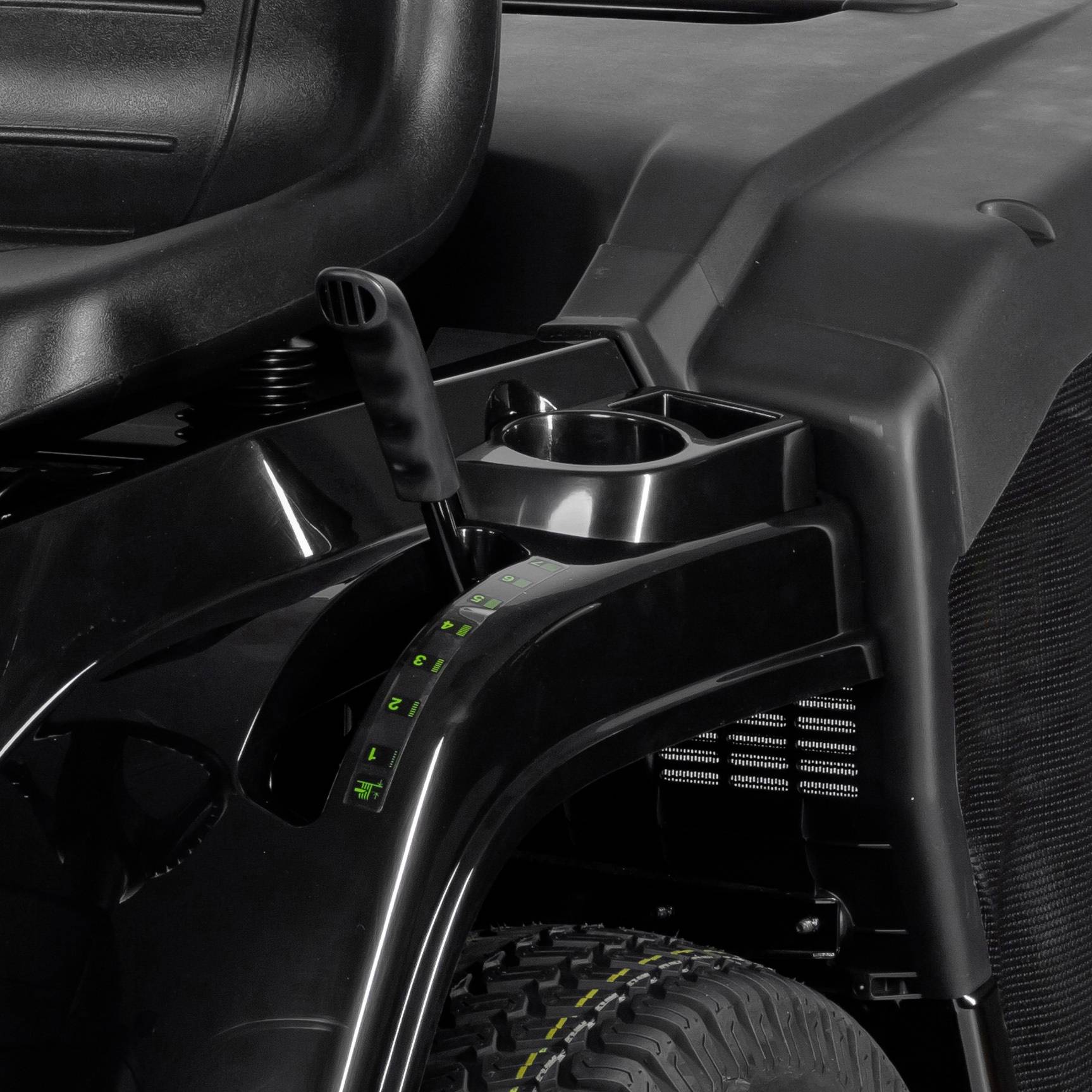 Nahaufnahme eines Sitzes mit einer Armlehne, einem Getränkehalter und dem Griff einer Steuerkonsole neben einem Vorderreifen.