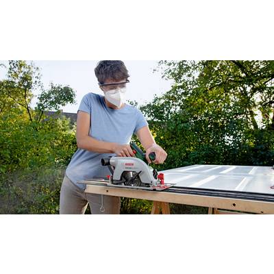 Eine Person trägt eine Schutzmaske und -brille und schneidet mit einer Kreissäge Holz auf einem Tisch im Freien.