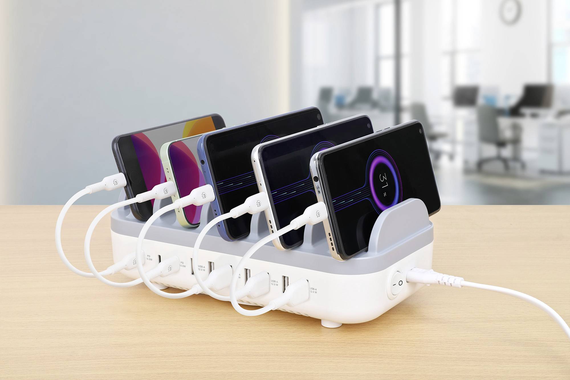 Mehrere Smartphones werden gleichzeitig an einer Ladestation aufgeladen. Im Hintergrund ist ein unscharfes Büro zu sehen.