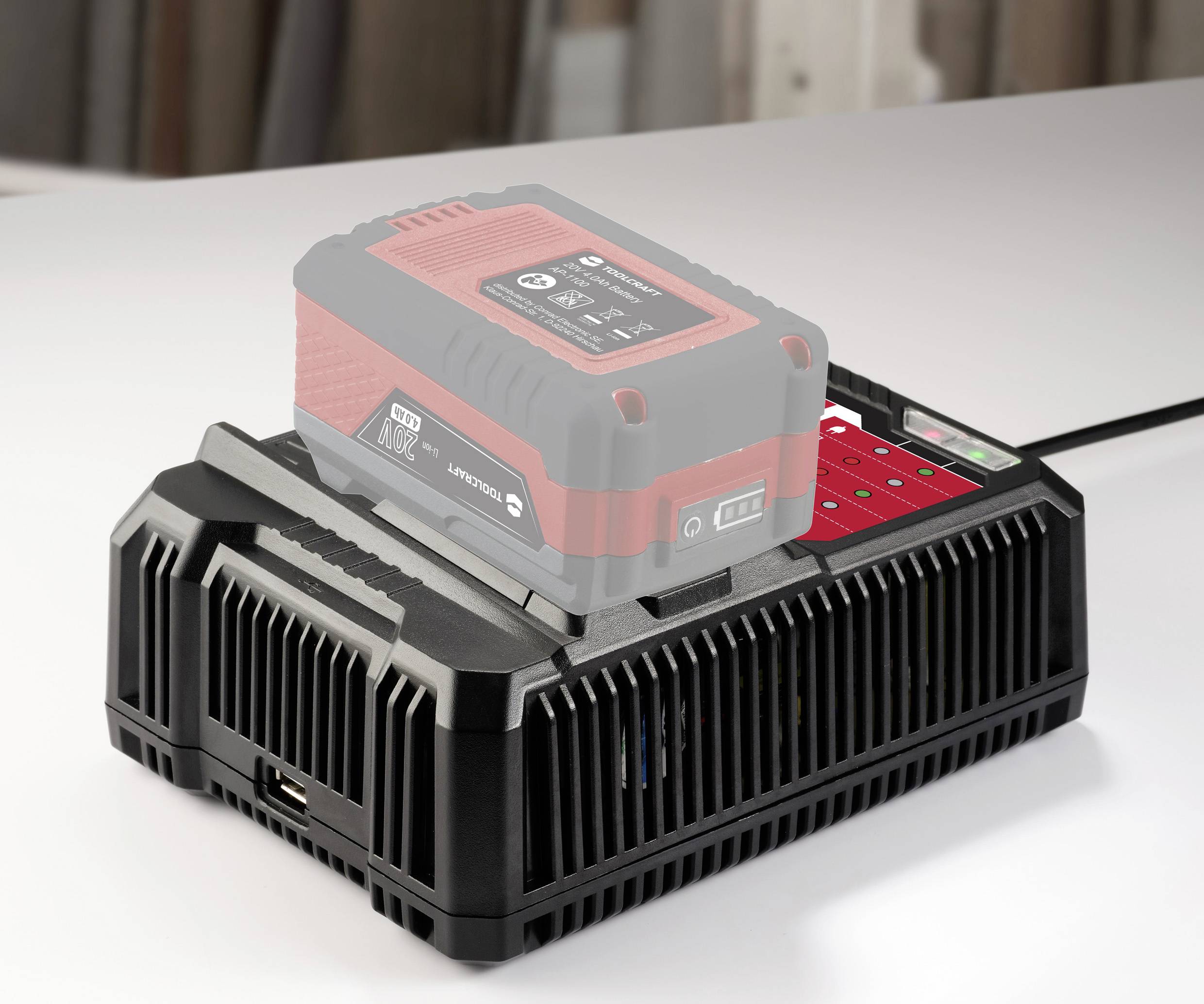 Ein roter Akku wird auf einer schwarzen Ladestation aufgeladen. Die Ladestation zeigt eine Ladeanzeige mit mehreren rot leuchtenden Punkten.