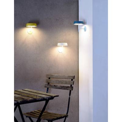 Drei moderne Wandleuchten in Grün, Weiß und Blau erhellen eine graue Wand über einem klappbaren Holztisch und Stuhl.