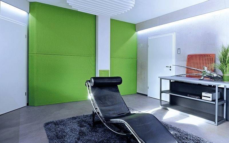 Ein modernes Zimmer mit einer schwarzen Liege auf einem grauen Teppich, grüner Wandverkleidung, weißen Wänden und einem Tisch rechts.