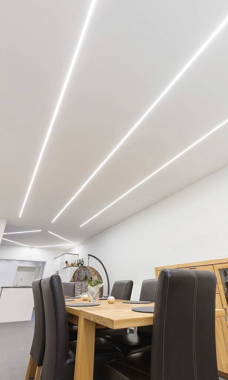Ein Esszimmer mit einem Holztisch und sechs Lederstühlen. Die Decke hat moderne, schmale LED-Leuchten, die den Raum erhellen.