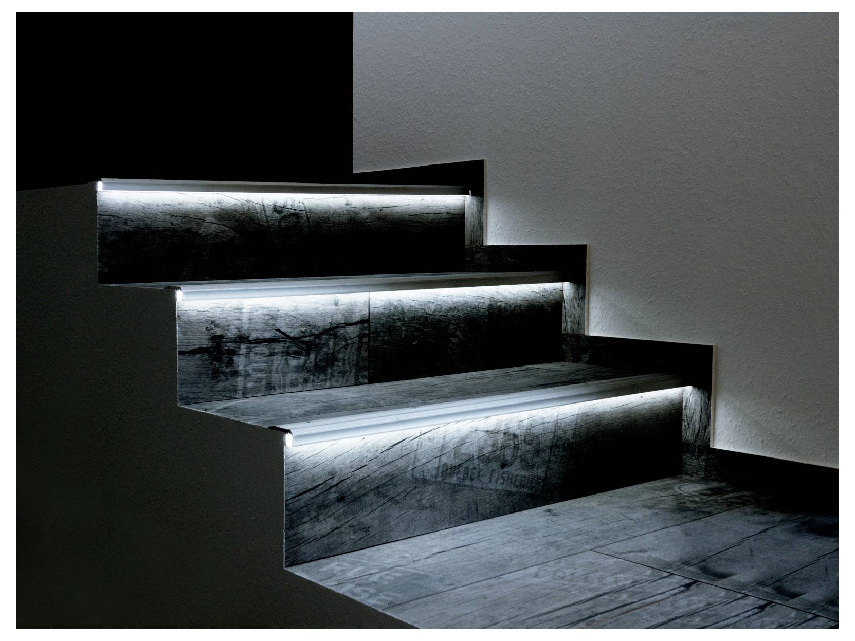 Moderne Treppe mit beleuchteten Stufenkanten und dunkelgrauen gefliesten Trittflächen vor einer minimalistischen schwarz-weißen Wandgestaltung.