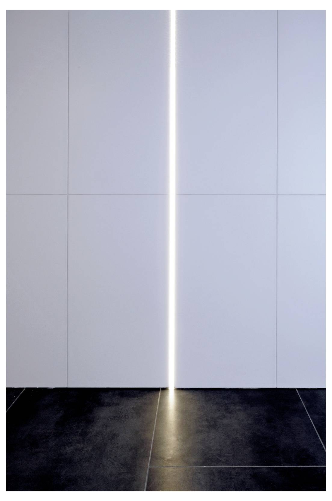 Minimalistischer Innenraum mit einem vertikalen Streifen hellen Lichts zwischen großen, hellen Wandpaneelen, der sich auf einem dunklen Fliesenboden spiegelt.