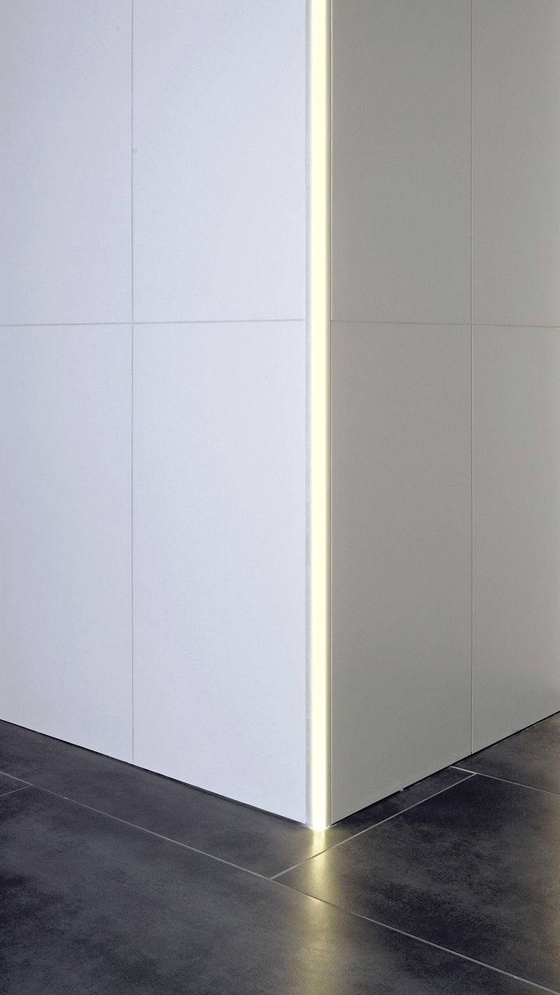 Weiße Ecke eines Raumes mit strukturierter Wand und grauem Boden. Ein schmaler, vertikaler Lichteffekt betont die Kante.