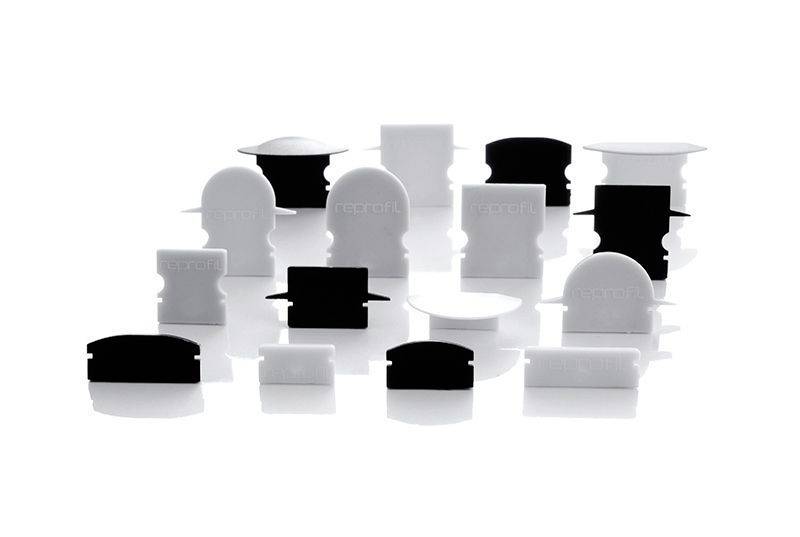 Verschiedene weiße und schwarze Kunststoffteile, geometrisch geformt, stehen auf einem reflektierenden Untergrund vor einem weißen Hintergrund.