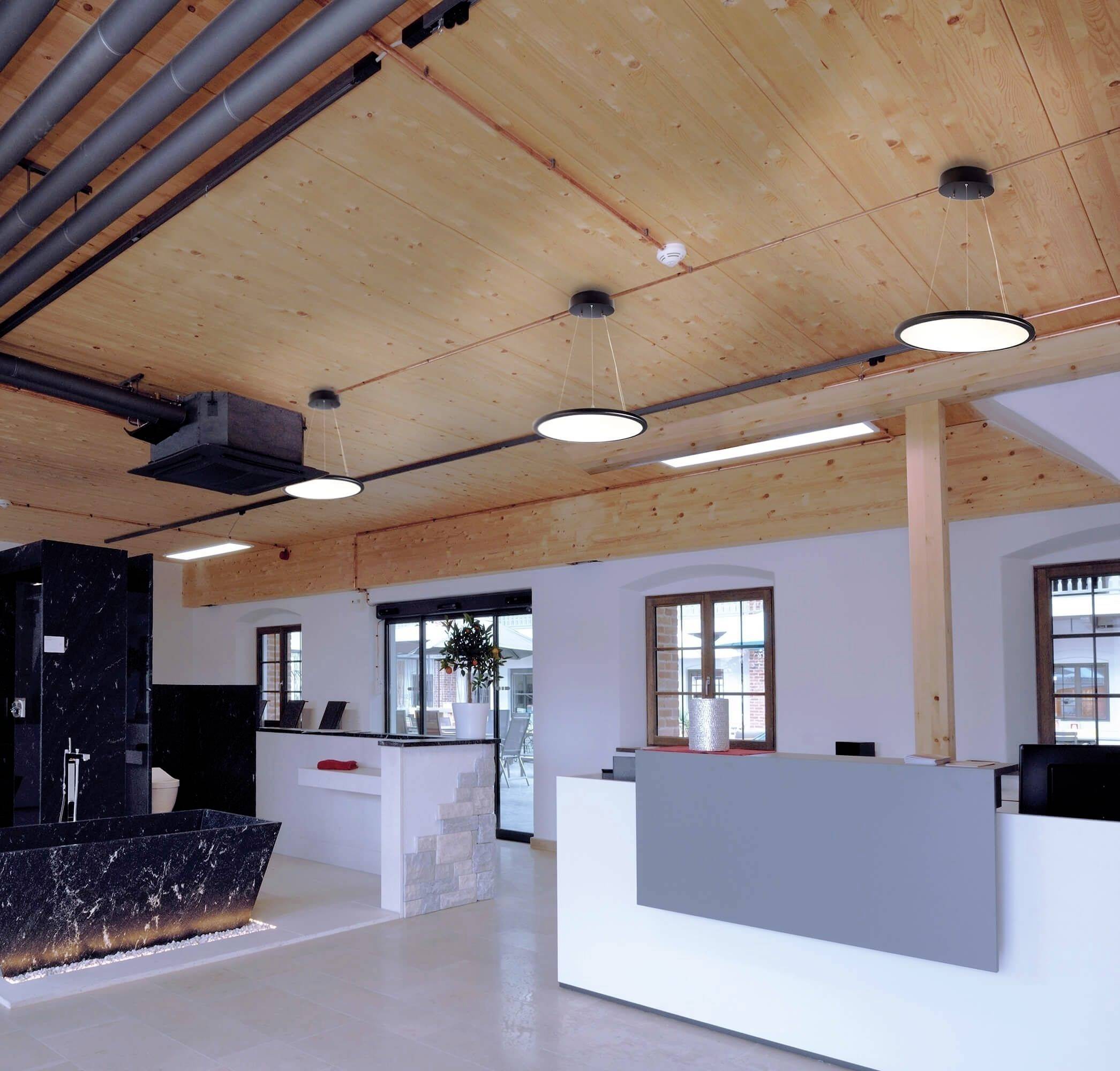 Ein modernes Büro mit Holzbalkendecke, hellen Wänden und einer Empfangstheke. Die Beleuchtung ist in die Decke integriert.