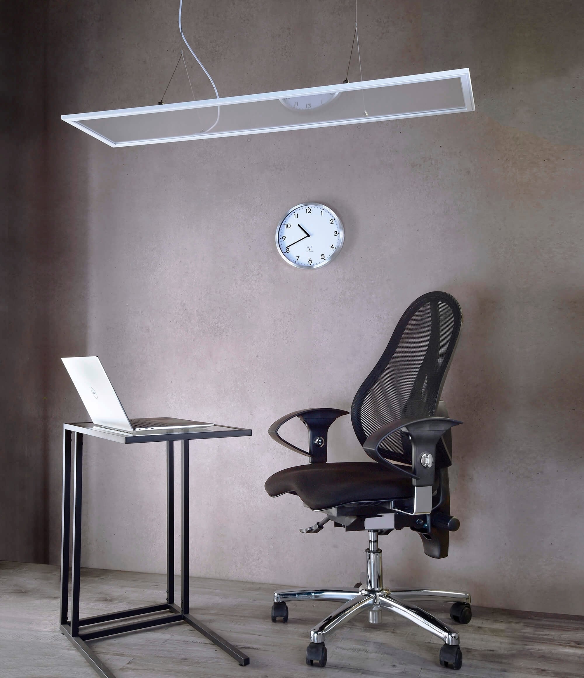 Moderner Arbeitsplatz mit einem Laptop auf einem schmalen Tisch, einem ergonomischen schwarzen Bürostuhl und einer Wanduhr in einem minimalistischen Raum.