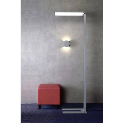 Eine moderne, freistehende Lampe leuchtet eine graue Wand an. Daneben steht ein roter Hocker, der Kontrast zum schlichten Design bietet.