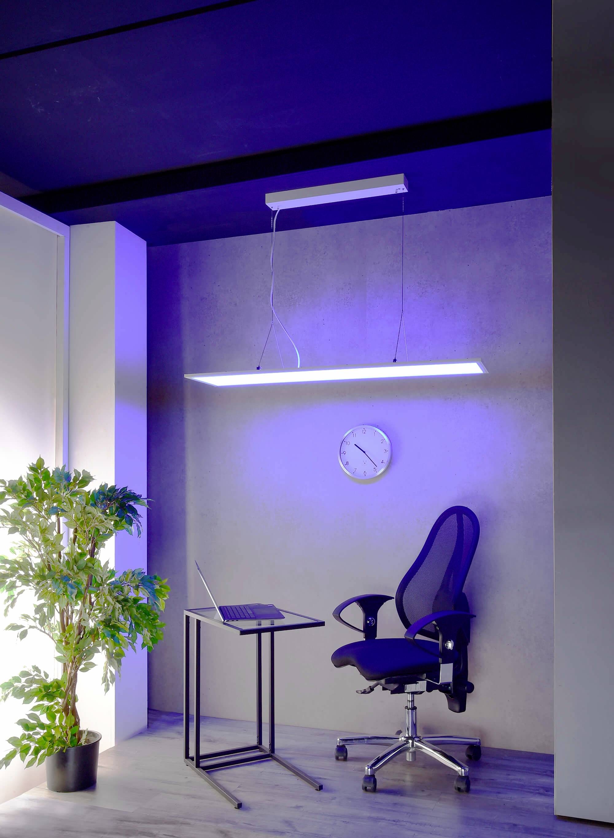 Ein moderner Arbeitsplatz mit schwarzem Bürostuhl, kleinem Tisch mit Laptop, LED-Leuchte an der Decke, Wanduhr und Pflanze.