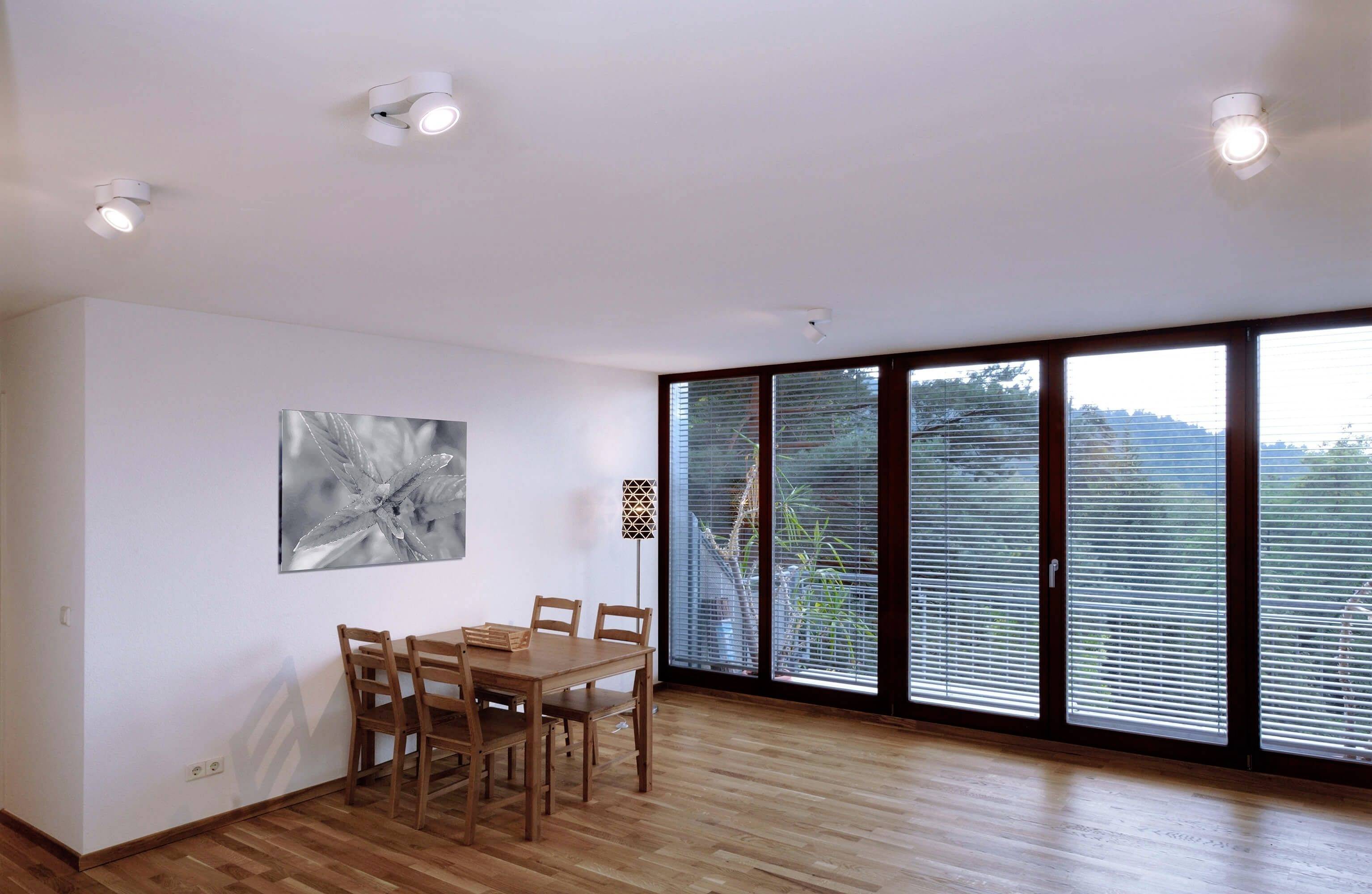Ein moderner Essbereich mit Holztisch und Stühlen. Große Fenster mit Ausblick auf bewaldete Hügel. Dezente Beleuchtung und helle Wände.