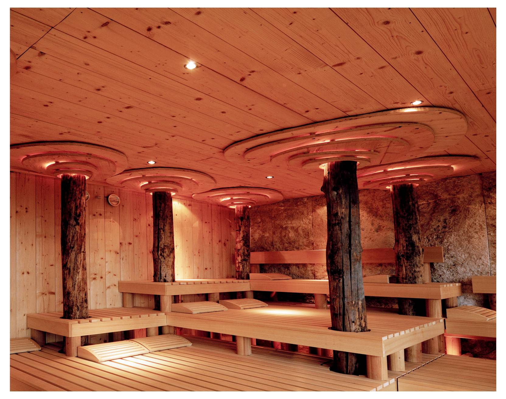 Leere Holzsauna mit gestuften Bänken und Holzsäulen unter warmem orangefarbenem Licht