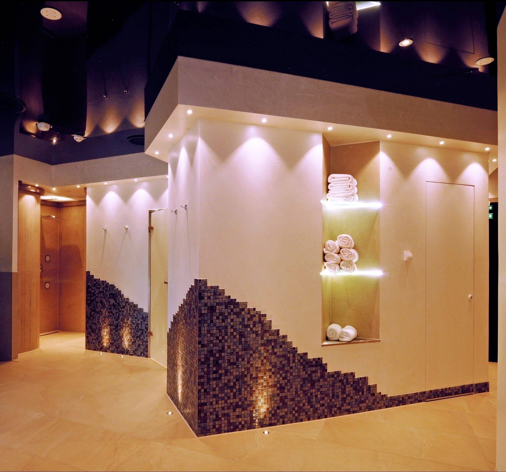 Ein stilvoller Innenraum eines Spas mit weichen Beleuchtungen und modernen, minimalistischen Design; Handtücher sind ordentlich gestapelt.