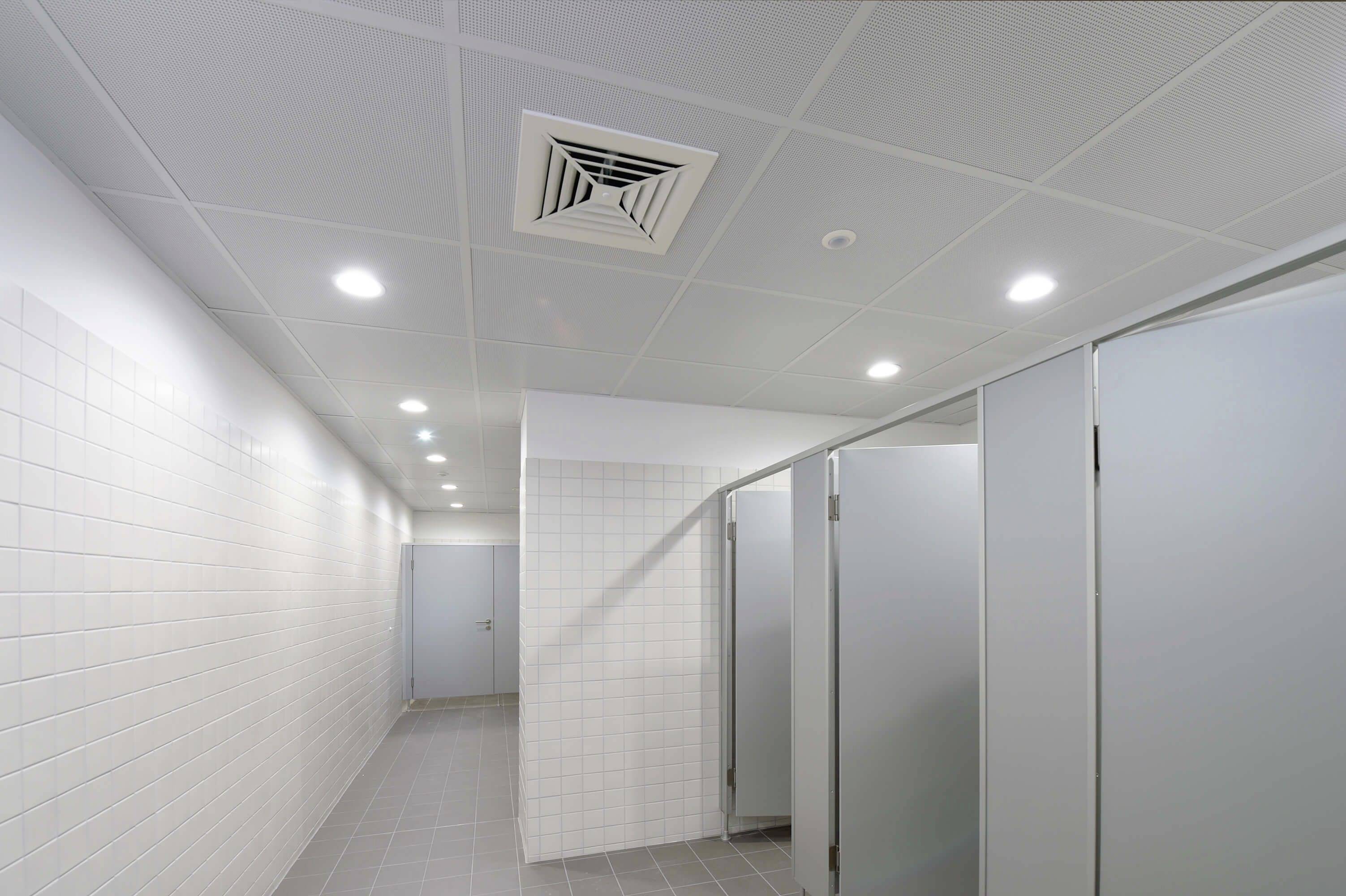 Helle, geflieste öffentliche Toilettenanlage mit mehreren geschlossenen Kabinen und Deckenbeleuchtung.