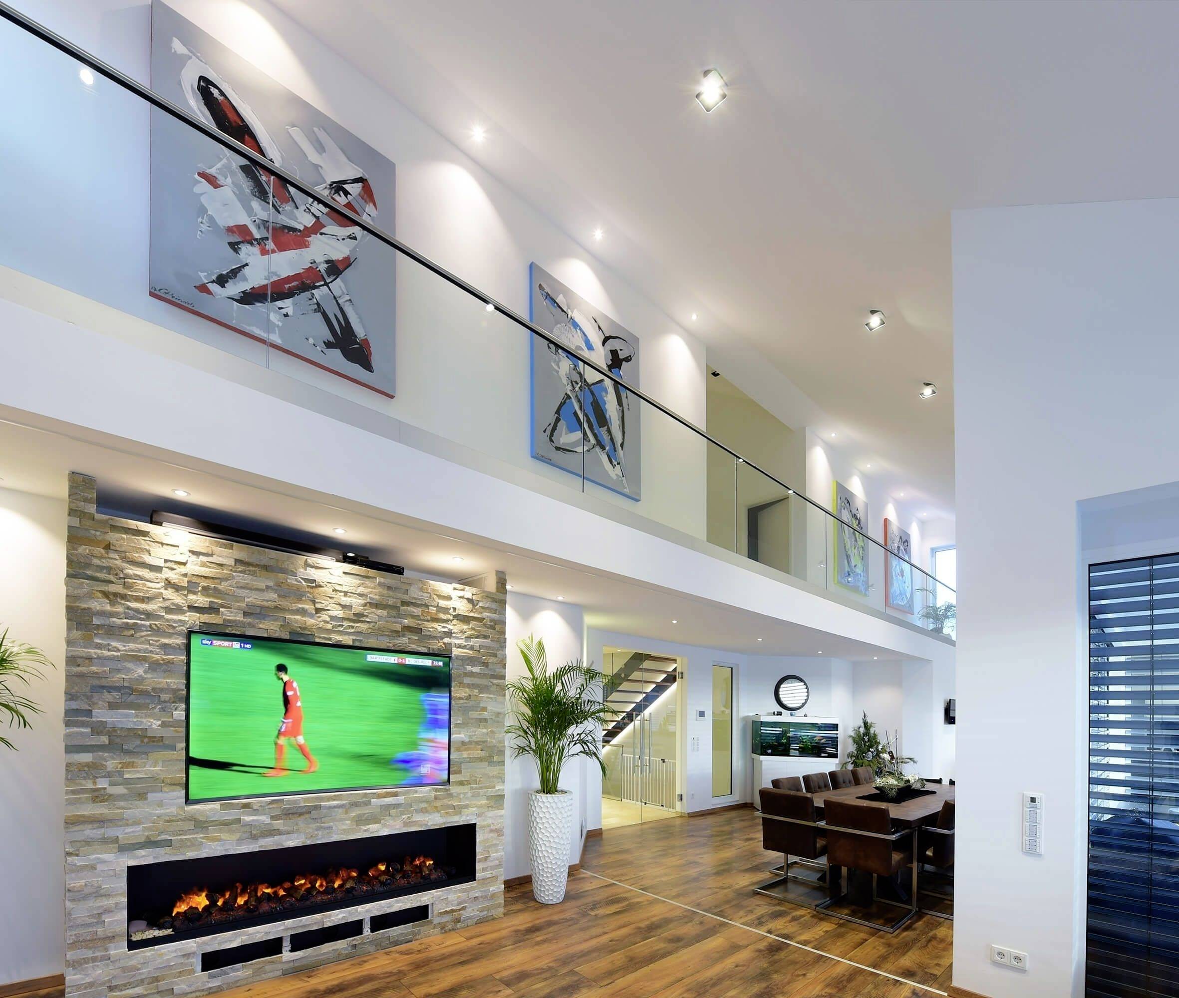 Modernes Wohnzimmer mit Holzboden, einer großen Wand mit Kunstwerken und einem Fernseher, der ein Fußballspiel zeigt. Elegante Einrichtung.