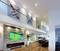 Modernes Wohnzimmer mit Holzboden, einer großen Wand mit Kunstwerken und einem Fernseher, der ein Fußballspiel zeigt. Elegante Einrichtung.