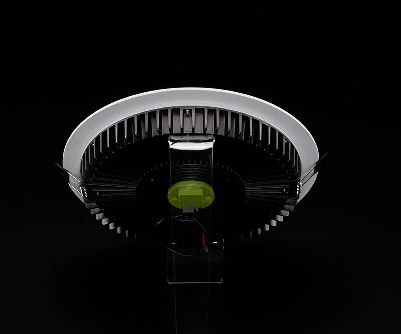 Ein rundes, modernes LED-Licht mit Kühlrippen aus schwarzem Metall, auf einem transparenten Ständer vor schwarzem Hintergrund.