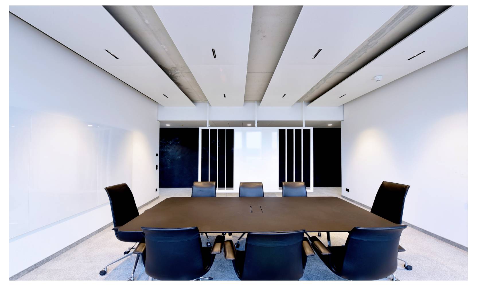 Modernes Konferenzraum mit einem langen Tisch und acht Stühlen, mit Blick auf eine Wand aus Schiebepaneelen oder Bildschirmen in einer minimalistischen Büroumgebung.