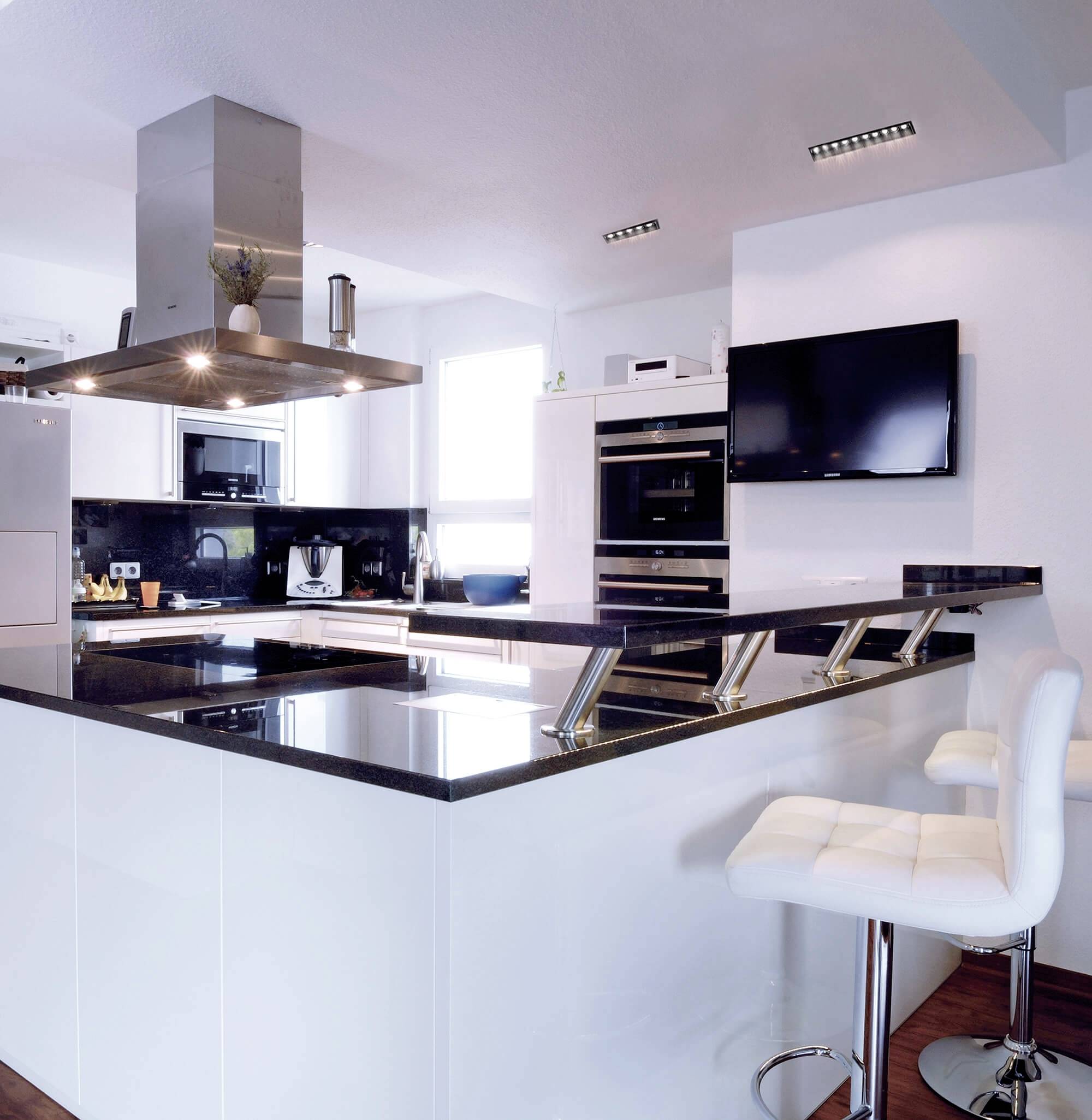 Moderne Küche mit einer Insel aus schwarzem Marmor, weißen Schränken und Barhockern. Helle Beleuchtung und eingebauter Backofen.