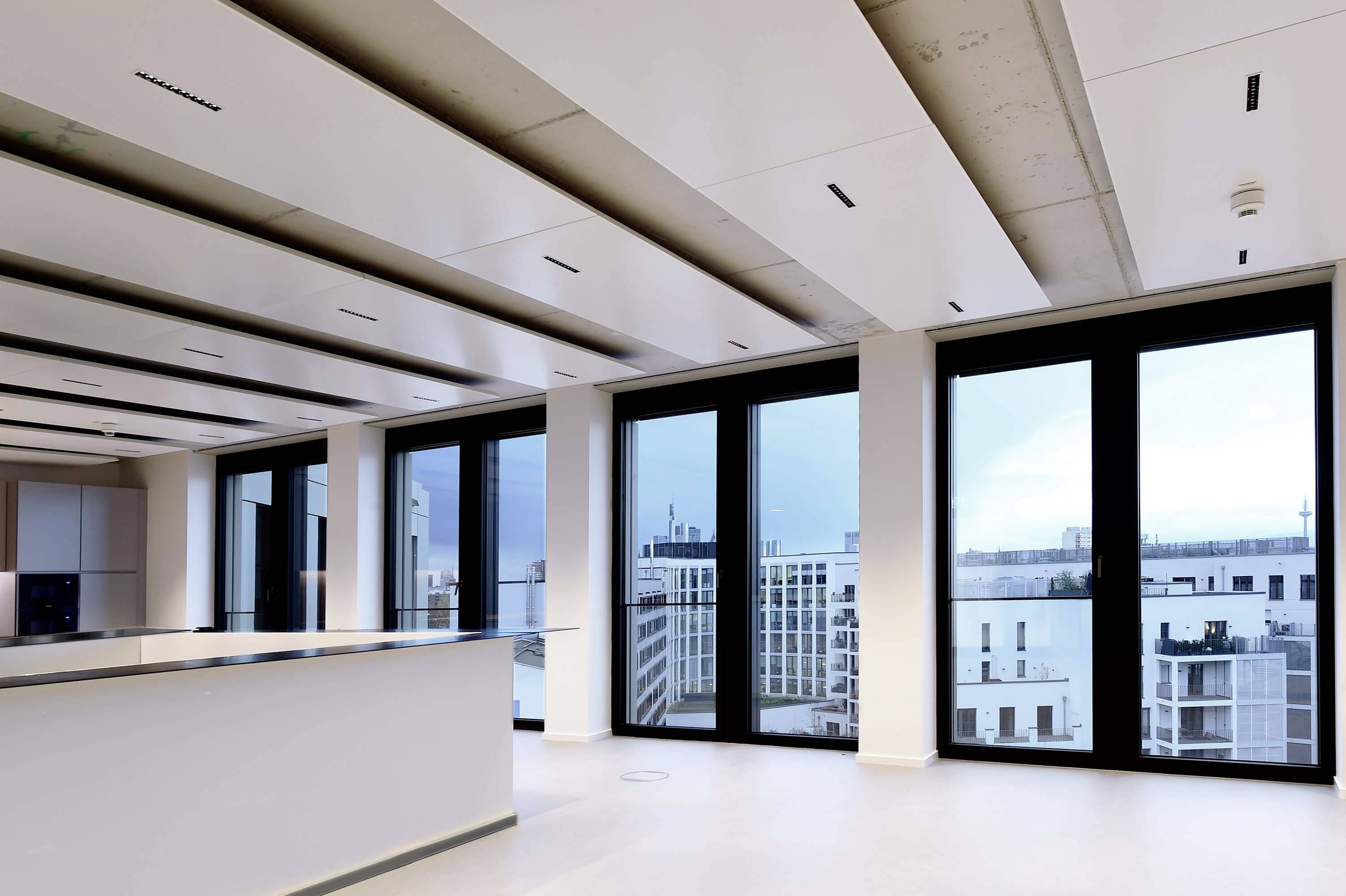 Blick aus einem modernen, offenen Büro mit großen Fenstern, die eine urbane Skyline bei bewölktem Himmel zeigen.