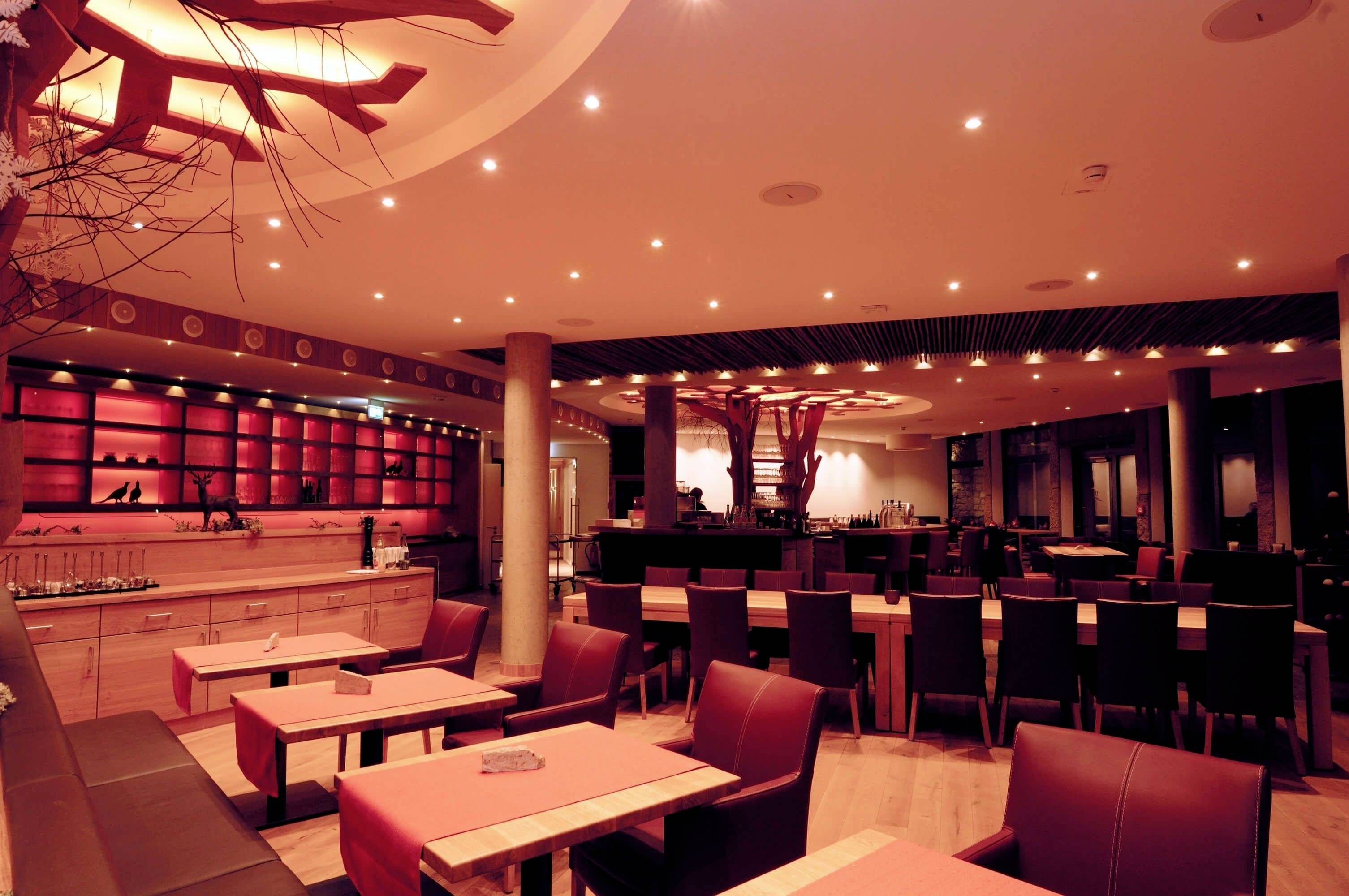 Ein modern eingerichtetes Restaurant mit Holztischen und -stühlen, warmem Licht und einer dekorativen Deckenbeleuchtung.