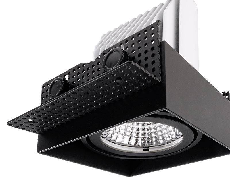 Ein Deckenstrahler mit quadratischem Rahmen in schwarzer Farbe, der an einer Unterkonstruktion montiert ist. Die Lampe hat ein Gittermuster und silberne Kühlrippen.