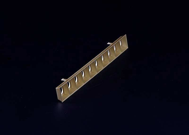 Ein schmaler, goldener rechteckiger Gegenstand mit mehreren nebeneinander liegenden Öffnungen, freigestellt auf schwarzem Hintergrund.