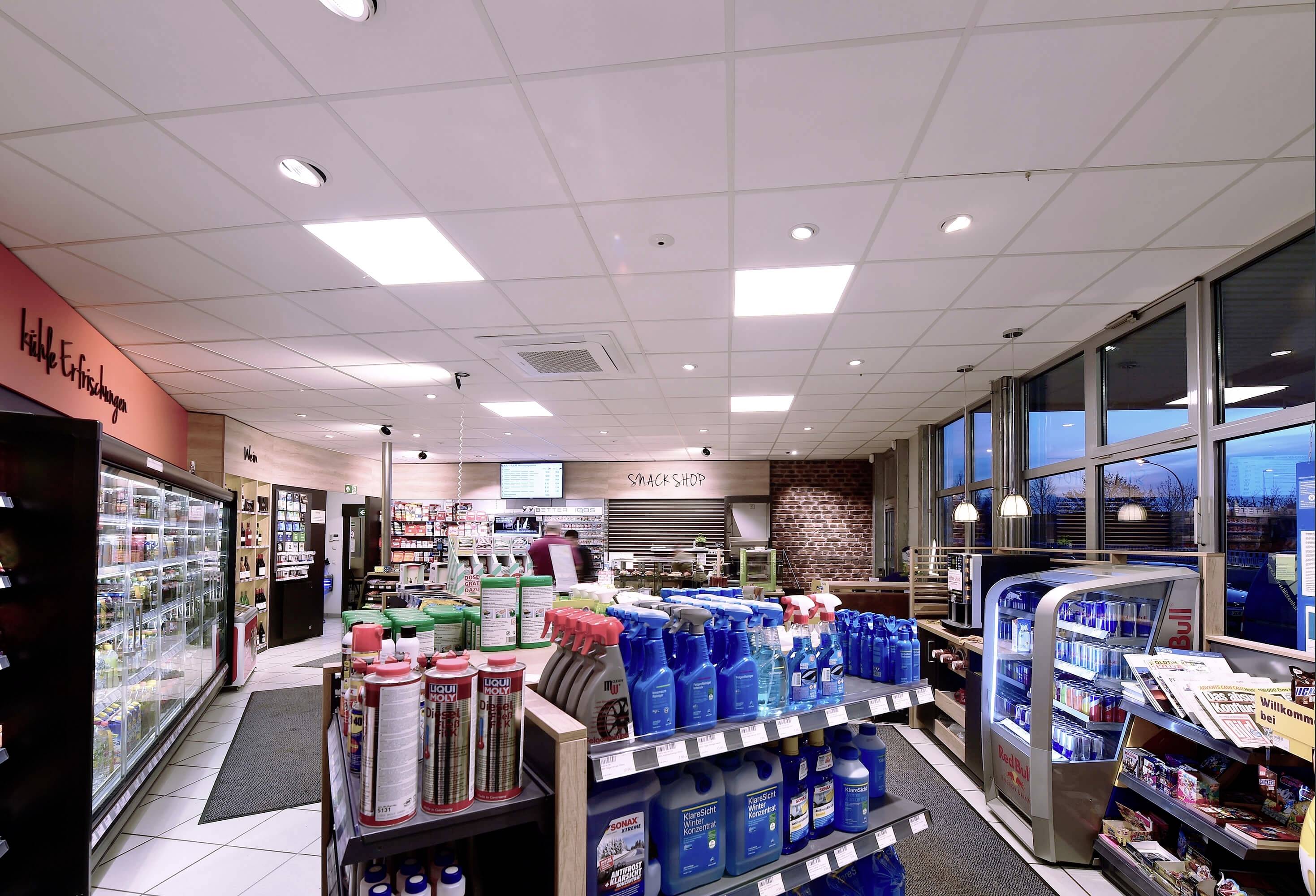 Ein gut beleuchteter Tankstellenshop mit Regalen voller Produkte wie Reinigungsmittel und Snacks. Ein Kühlschrank ist links sichtbar.