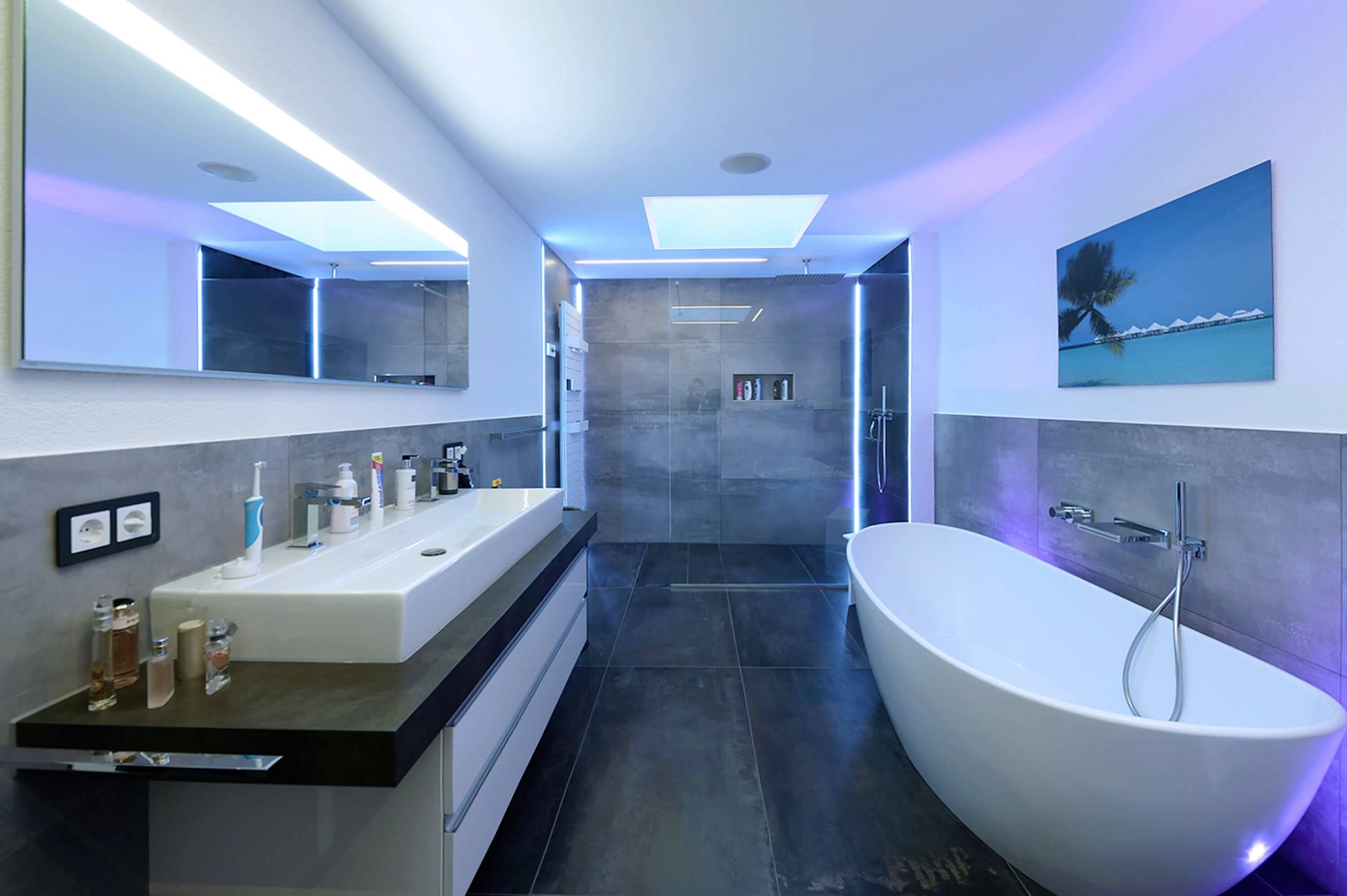 Modernes Badezimmer mit freistehender Badewanne, großem Spiegel, Waschbecken mit Pflegeprodukten und gedämpfter blauer Beleuchtung.