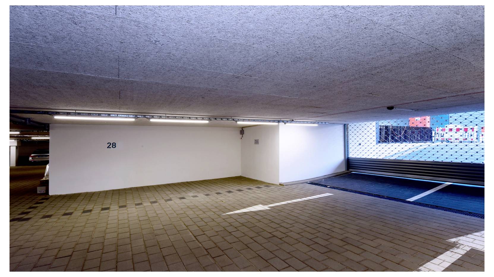 Leerer Innenparkplatz mit nummerierter Wand „28“, gefliestem Boden und einem Ausgang auf der rechten Seite.