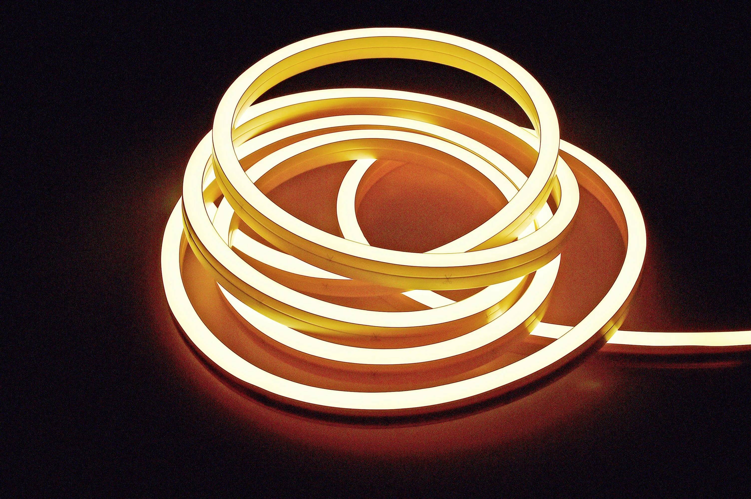 Ein zusammengerollter LED-Lichtstreifen leuchtet in warmem Weiß auf dunklem Hintergrund und bildet spiralförmige Muster.