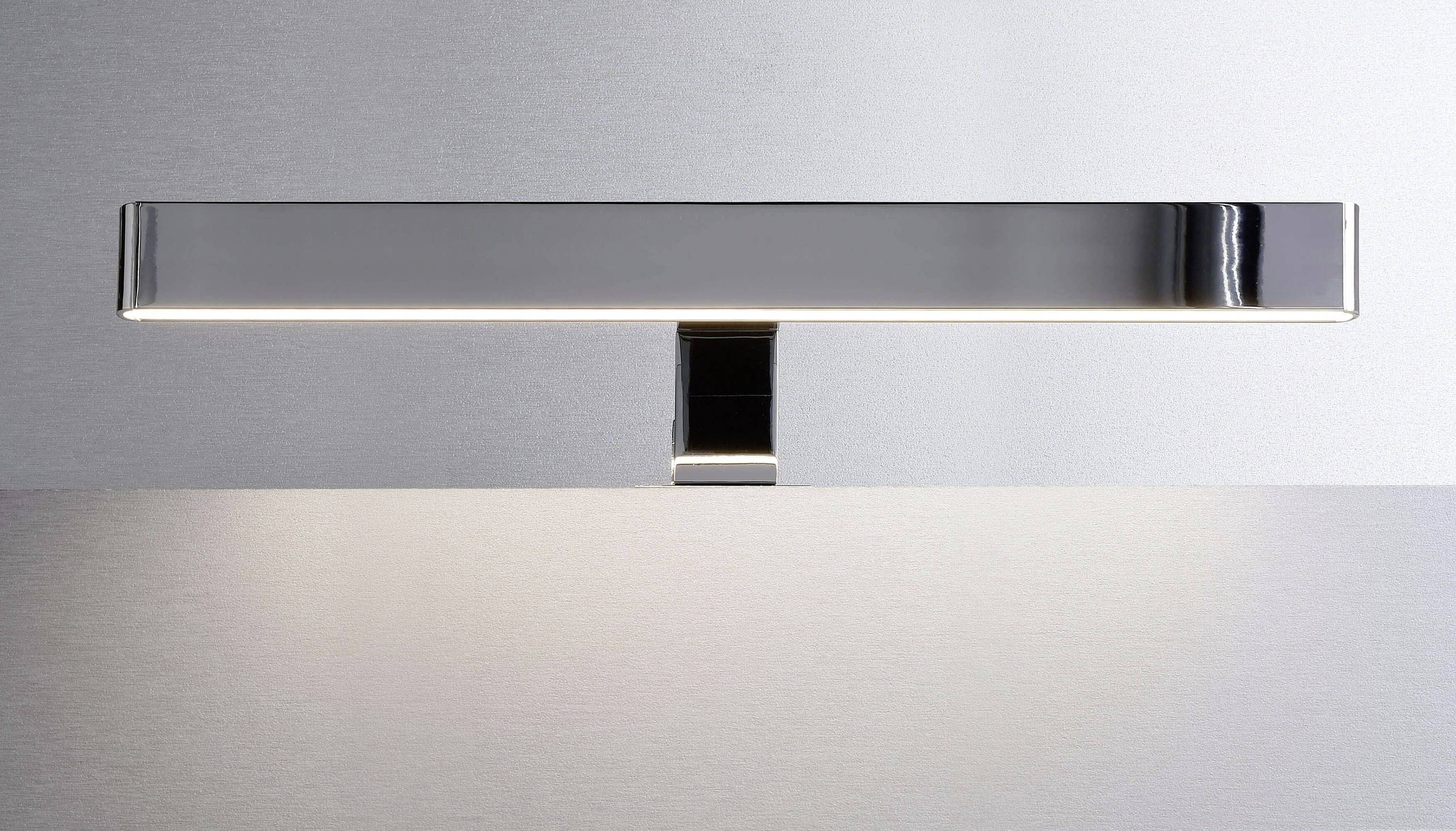 Silberne Wandleuchte mit modernem, minimalistischem Design, leuchtet gleichmäßig nach unten auf eine glatte, graue Oberfläche.