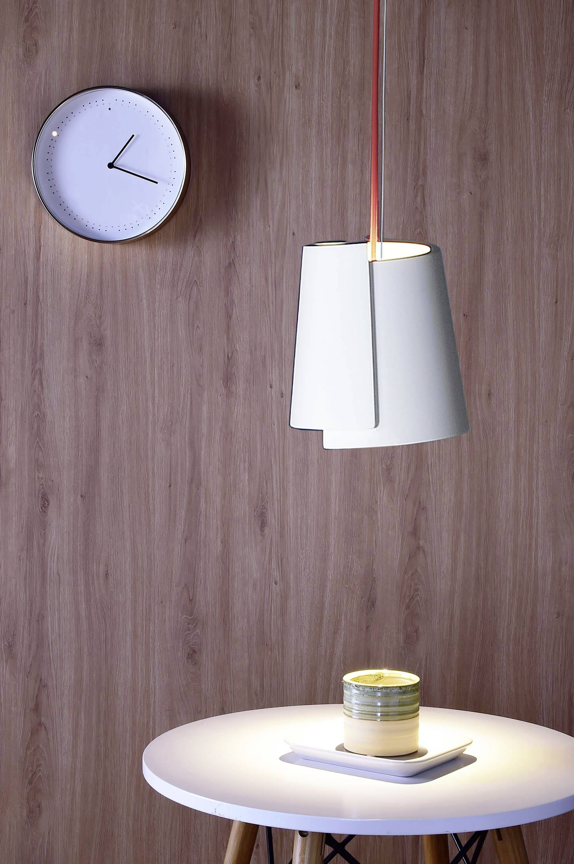Beleuchteter Tisch mit Kerze, moderne Hängelampe und Uhr an holzverkleideter Wand. Minimalistische Einrichtung.