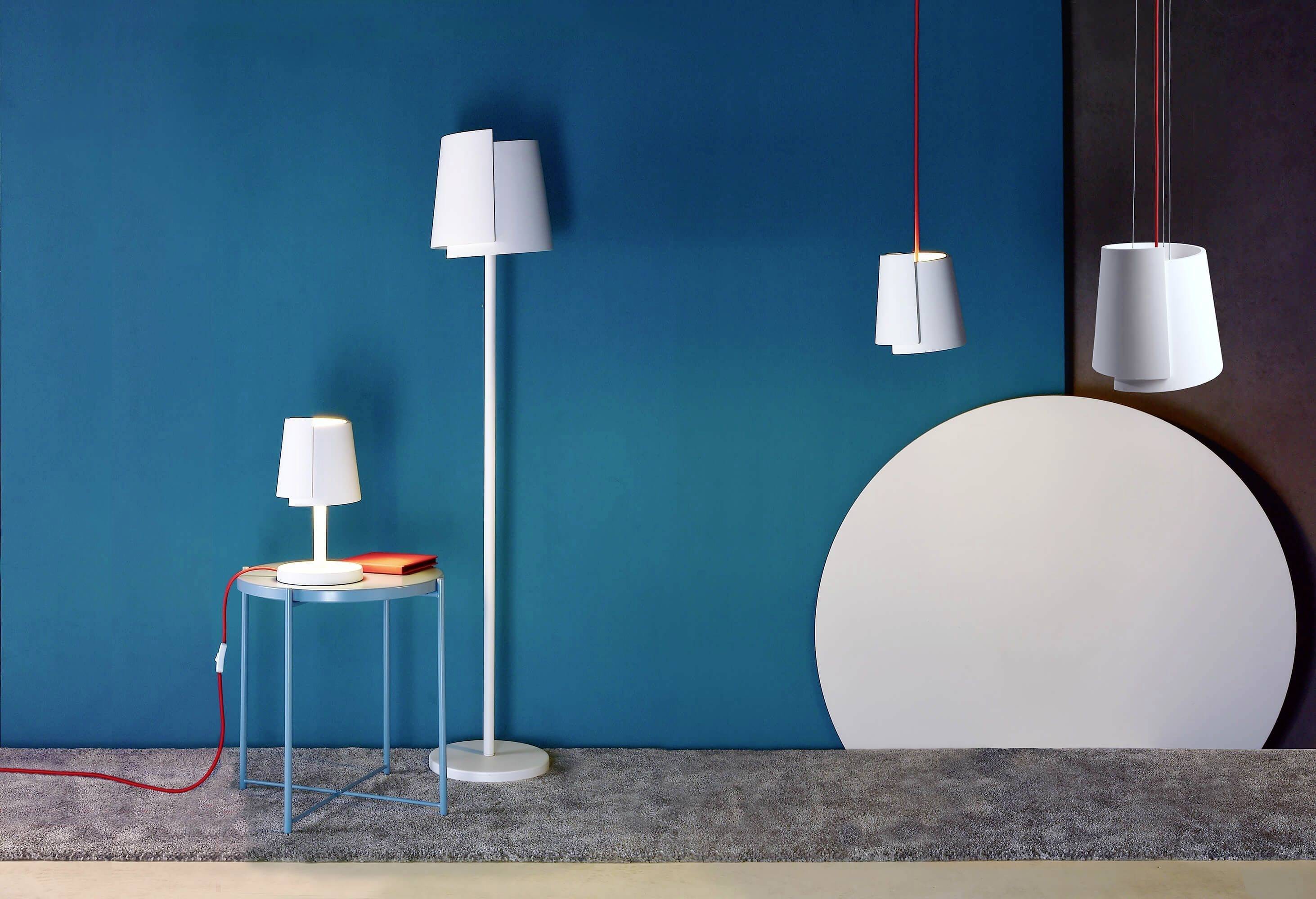 Eine moderne Lampe in verschiedenen Größen auf einem Teppich vor einer blauen Wand und einem runden, weißen Objekt.