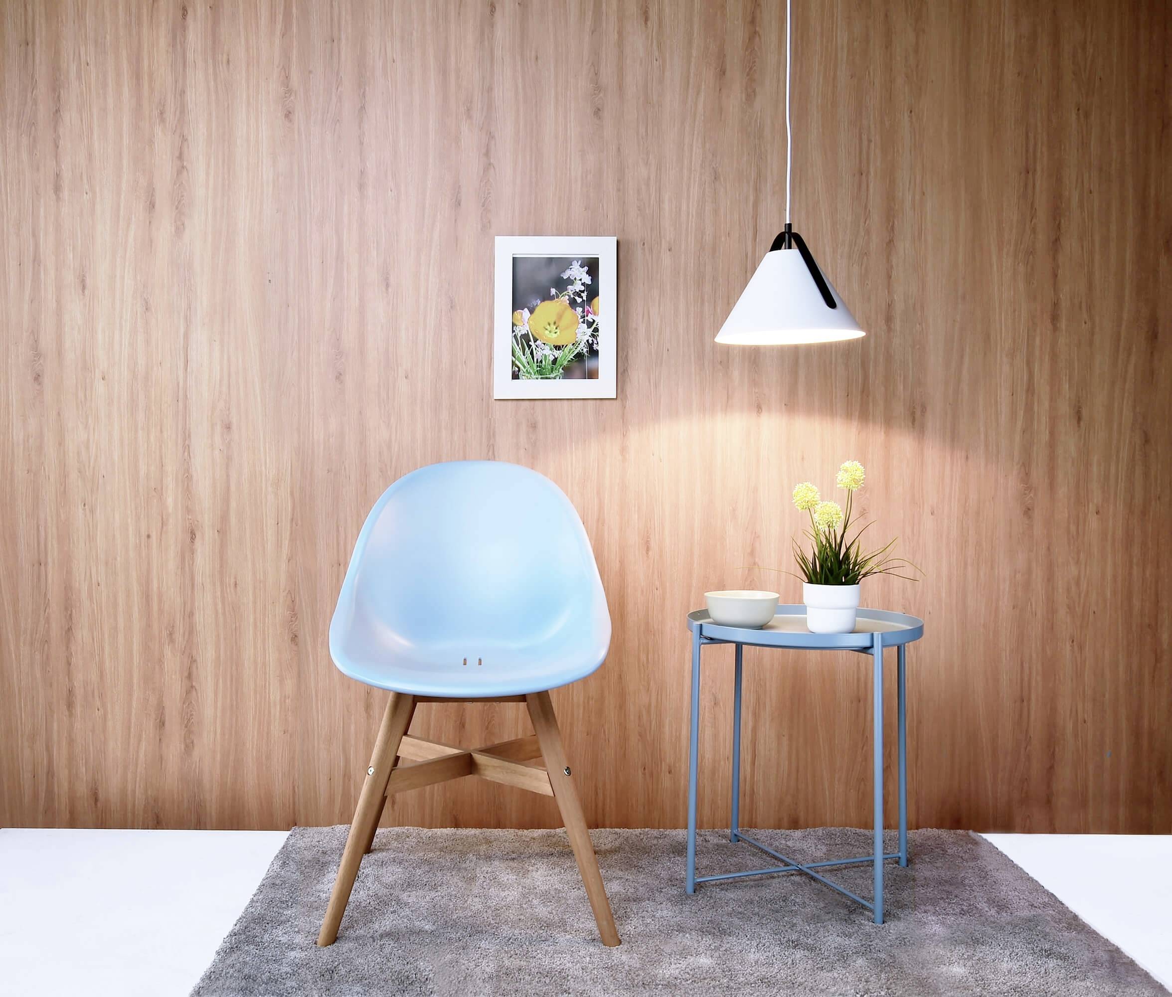 Blaue Stuhl und Tischarrangement vor Holzwand mit Bild, Lampe und Blumendekor auf grauem Teppich. Minimalistisches Interieur.