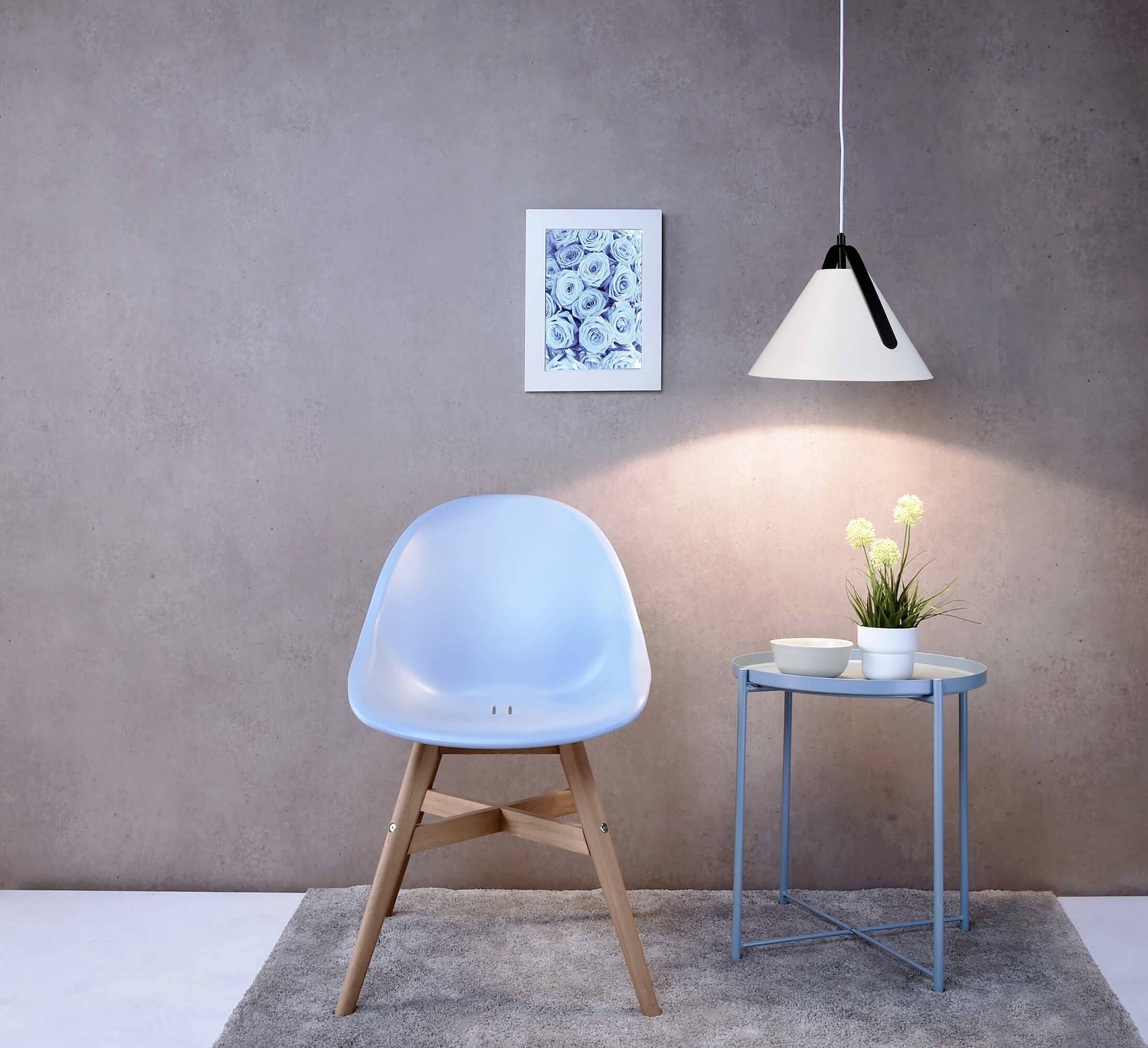 Hellblaue Stuhl vor neutraler Wand, daneben runder Tisch mit Pflanze und Lampe darüber, wandhängendes Bild im Hintergrund.