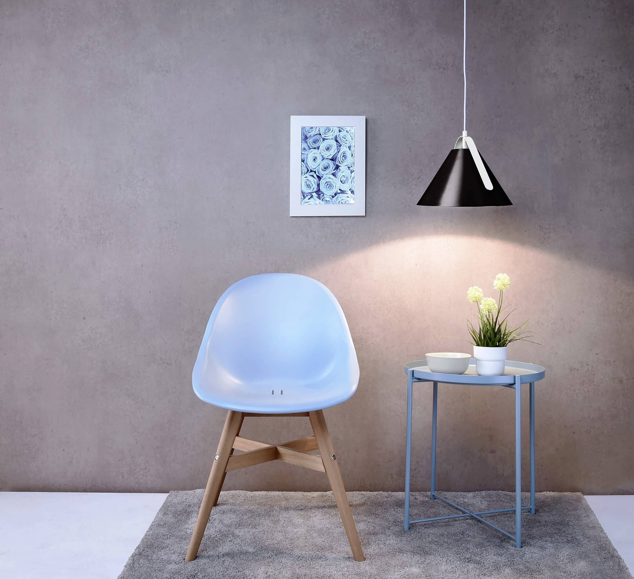 Ein hellblauer Stuhl steht auf einem grauen Teppich neben einem kleinen blauen Tisch mit Pflanzen und einer Hängelampe an der grauen Wand.