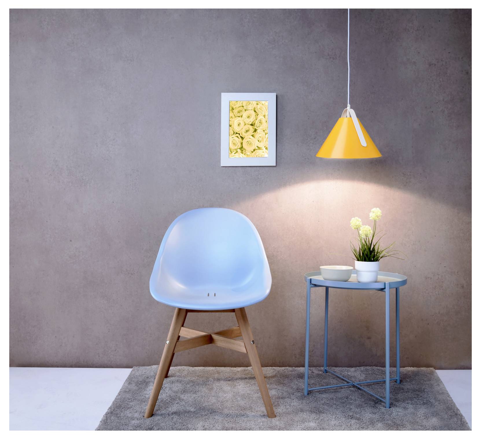 Moderner Innenraum mit einem blauen Sessel, einem kleinen Beistelltisch mit Blumen, einer hängenden orangefarbenen Lampe und gerahmter Wandkunst vor einer grauen Wand.