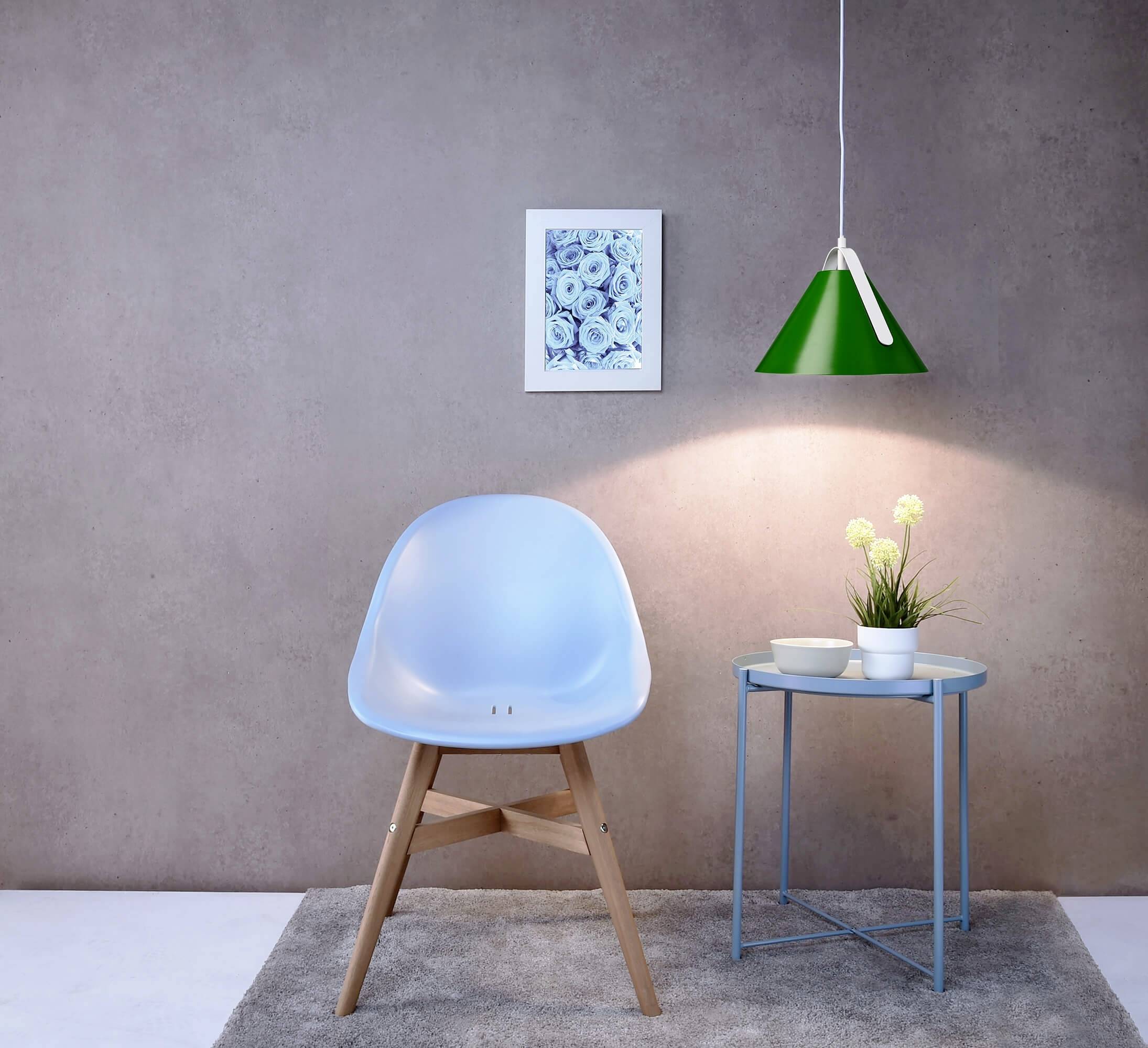 Ein blaues Designstuhl steht auf einem grauen Teppich neben einem runden Beistelltisch mit Pflanze und Schalen, beleuchtet durch eine grüne Lampe.