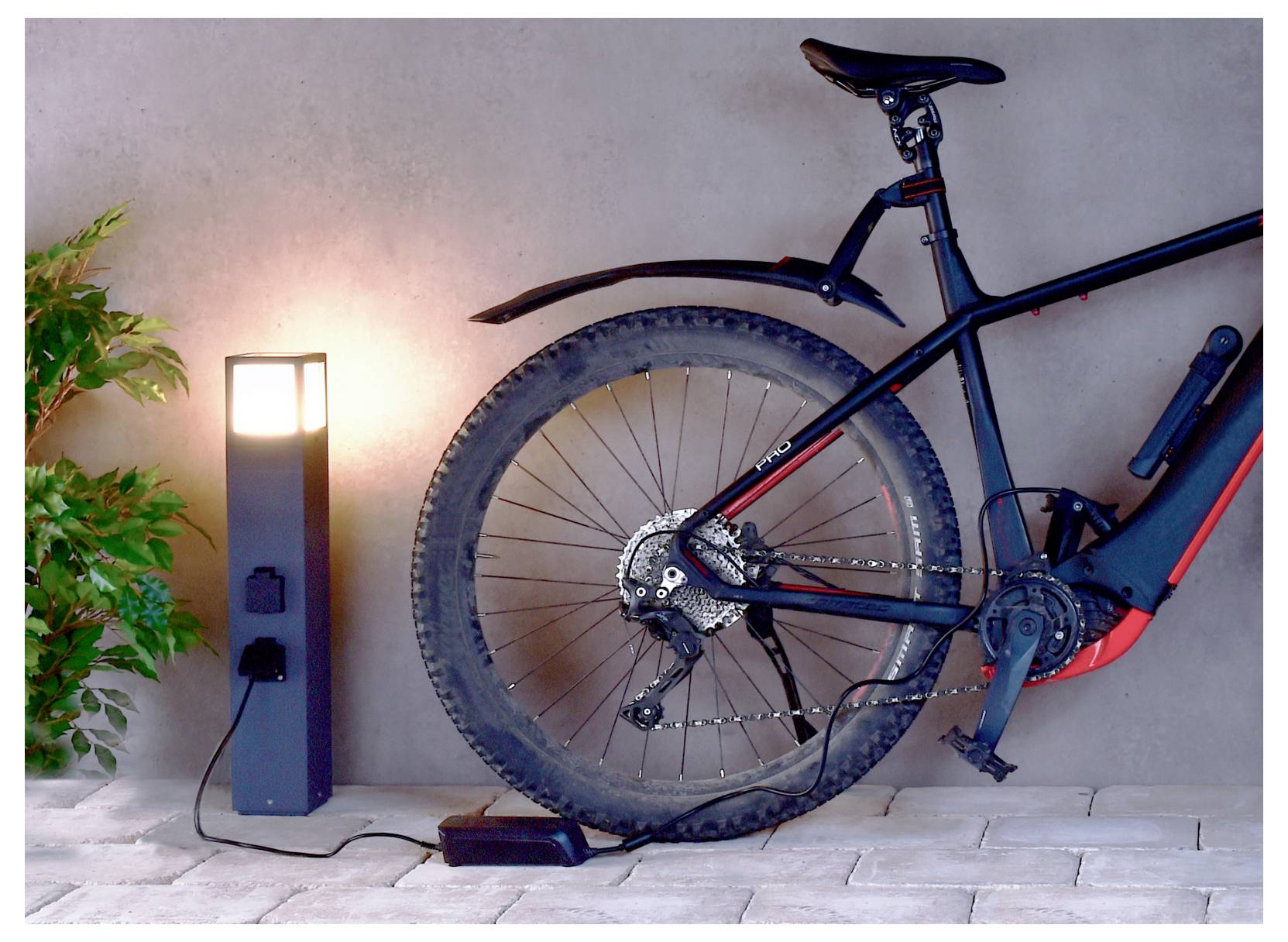 Elektrische Bodenleuchte neben einem Mountainbike, wobei Hinterrad und Rahmen vor einer Wand zu sehen sind.