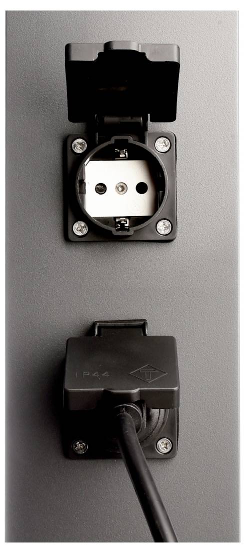 Geschlossene schwarze Außensteckdose mit wetterfesten Abdeckungen, ein Stecker steckt in der unteren Buchse an einer grauen Wand.