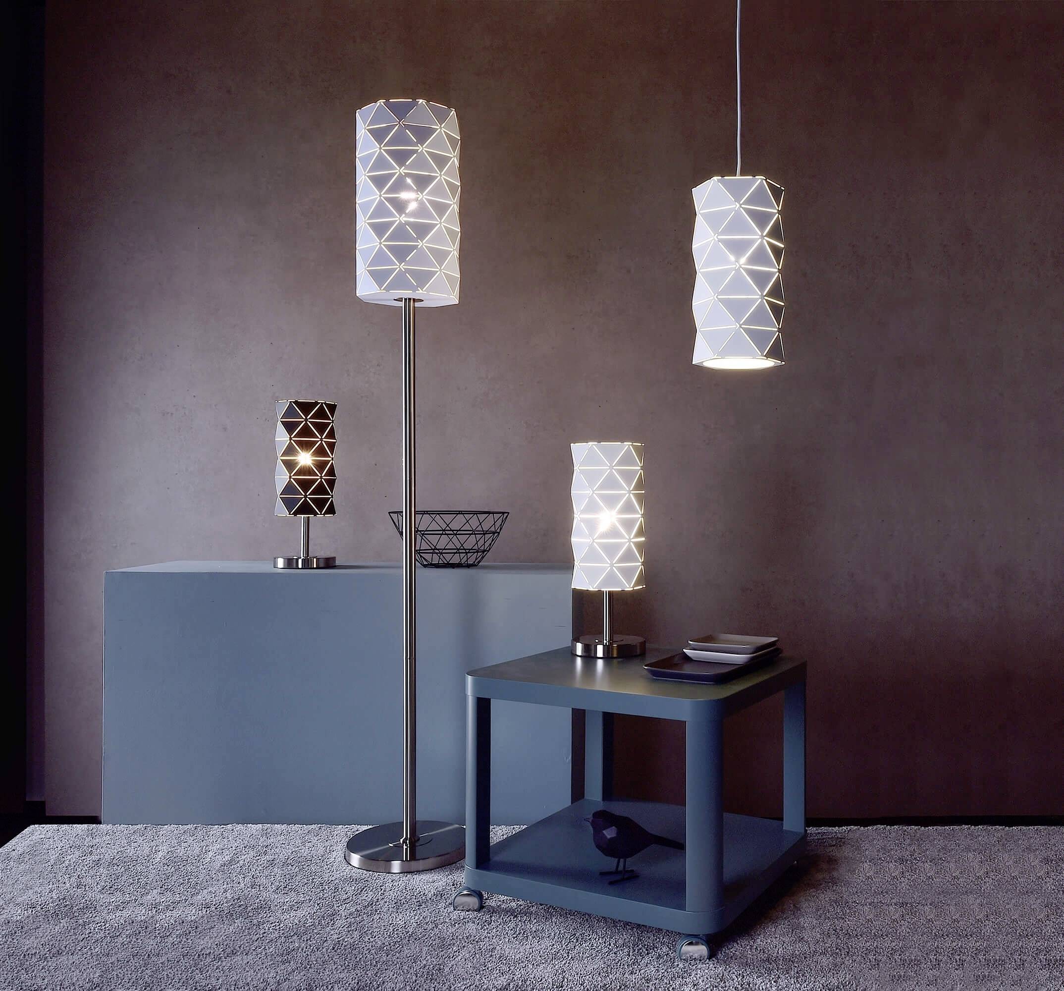 Mehrere moderne Lampen mit geometrischen Mustern stehen auf einem Tisch und Boden in einem eleganten Raum mit gedämpfter Beleuchtung.